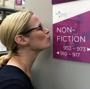 Editor pretending to kiss a sign that says "Nonfiction" on a library wall