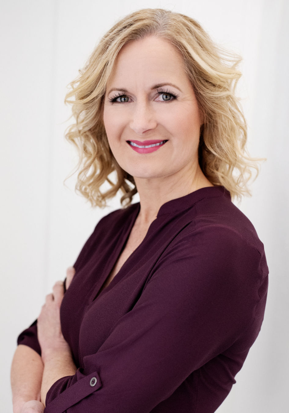 Jennifer smiling with her arms casually crossed, wearing a jacket and blouse over jeans